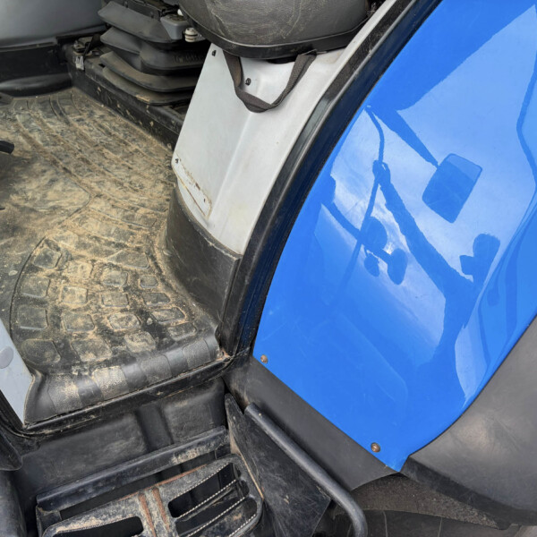 Interior of a blue vehicle cab showing a dirty rubber floor mat, pedals, and metal steps near the doorway.