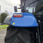 Close-up of a blue tractor front end with a large treaded tire and side mirrors, outdoors near a flag reading 'RUSSELLS'.