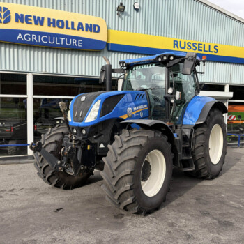 Blue New Holland tractor parked outside a dealership under a yellow-and-blue Russell sign