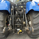 Blue tractor rear with large dual rear tires and exposed hydraulic hitch assembly.