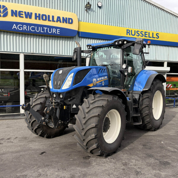 Blue New Holland tractor parked outside a dealership under a yellow-and-blue Russell sign