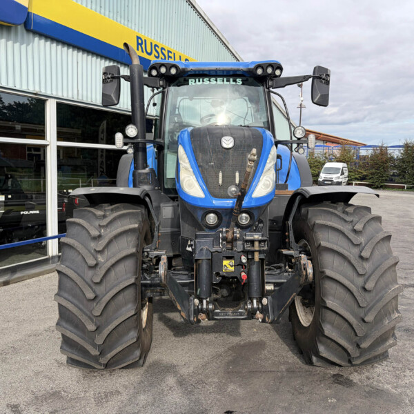 Blue farm tractor facing camera parked outside a dealership with large tires and a glass showroom window behind it - sign reads 'RUSSELLS'