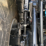 Close-up of a heavy-duty vehicle suspension with a coil spring and shock absorber among black chassis components.
