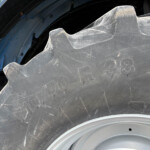 Close-up of a dusty truck tire and wheel rim, showing worn tread blocks and embossed markings on the rubber.