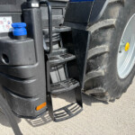 Close-up of a large agricultural tractor's front side with black plastic panels, steps, and a blue top-cap near the engine area.