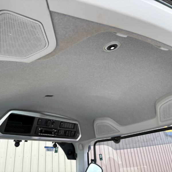 Interior view of a vehicle cab ceiling showing overhead speakers and a control panel near the windshield area.