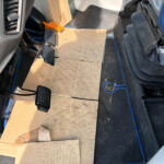 Cardboard mats laid over the car floor in the driver’s footwell, with pedals visible nearby.
