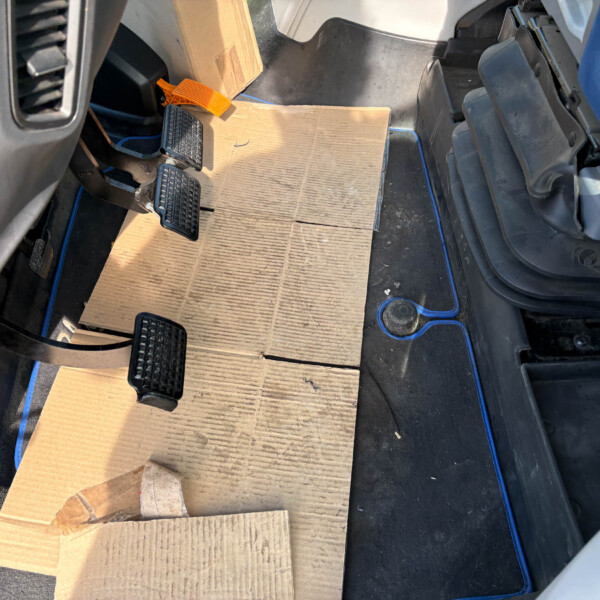 Cardboard mats laid over the car floor in the driver’s footwell, with pedals visible nearby.