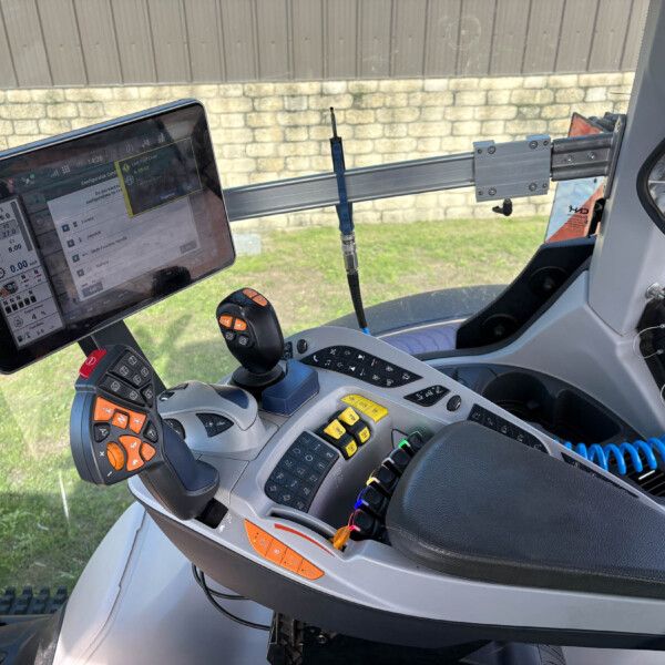 Inside a tractor cab showing a mounted touchscreen display, multiple joysticks and control levers on a gray dashboard.