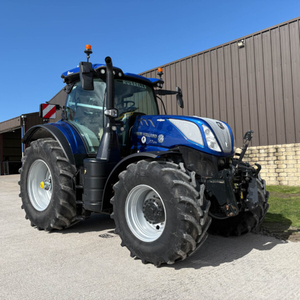 Blue New Holland tractor with oversized tires parked in front of a brown metal building under a clear blue sky