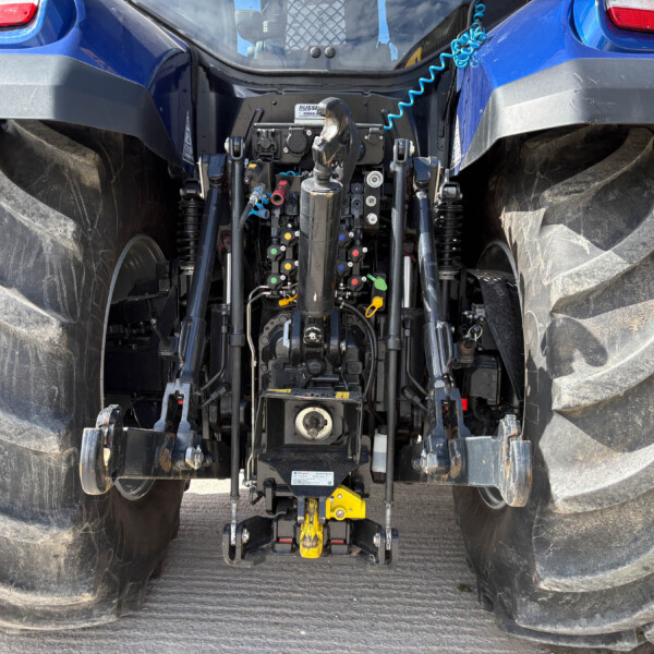 Blue tractor rear with exposed hydraulic valves and yellow three-point hitch between large muddy rear tires