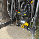 Close-up of a heavy-machine front-end hydraulic assembly with hoses, metal links, and yellow safety labels on a dirty tire side panel