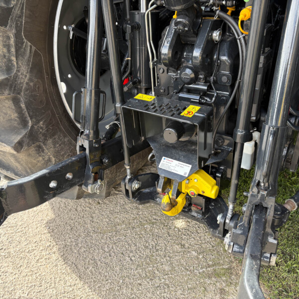 Close-up of a heavy-machine front-end hydraulic assembly with hoses, metal links, and yellow safety labels on a dirty tire side panel