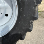 Close-up of a vehicle wheel and treaded tire, showing lug nuts and a gray rim, with an orange traffic cone in the background.