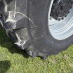 Close-up of a large off-road tire with a black sidewall and silver wheel on grass field.