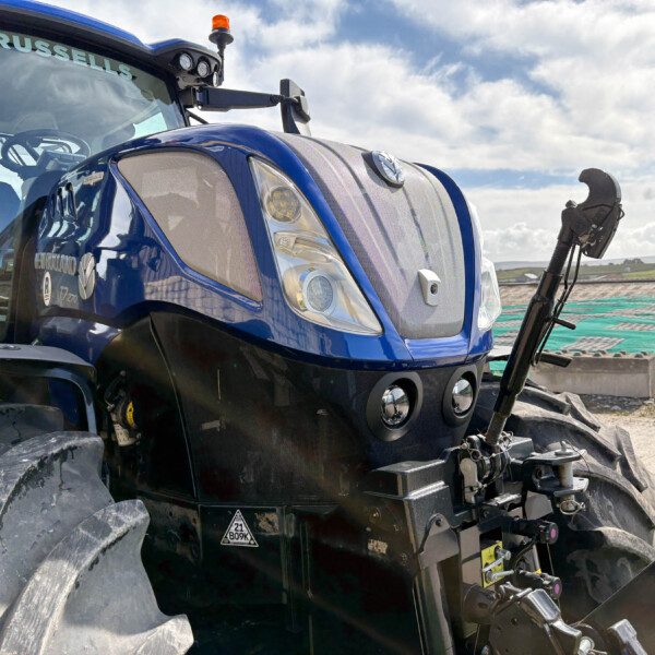 Close-up of a blue tractor front end with large treaded tires, chrome grille, and windshield showing 'RUSSELLS' against a cloudy sky