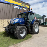 Blue New Holland tractor with oversized tires parked outside a dark metal building with a Russell’s sign.