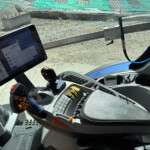 Cabin interior with a touchscreen tablet displaying controls, a joystick with orange buttons, and a panel of switches.",
