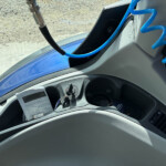 Interior of a vehicle cockpit with a bright blue coiled hose, ignition switch, and a printed manual on the dashboard edge.