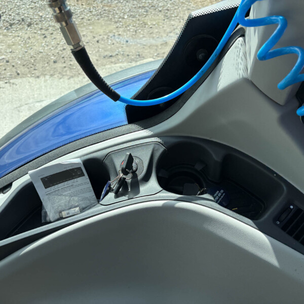 Interior of a vehicle cockpit with a bright blue coiled hose, ignition switch, and a printed manual on the dashboard edge.