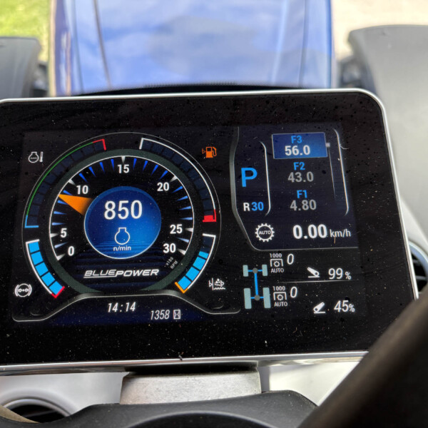Close-up of a car's digital instrument cluster: a circular gauge with blue accents, a central blue display, and small readouts for gear (P), fuel, and other indicators.