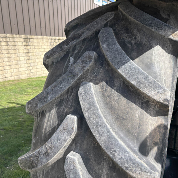 Close-up of a heavy-duty excavator/bucket with sharp, jagged teeth, dirty metallic surface, against a stone wall and grassy area background.