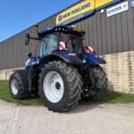 Blue New Holland tractor with oversized rear tires parked outside a building with a yellow New Holland Agriculture sign