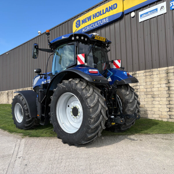 Blue New Holland tractor with oversized rear tires parked outside a building with a yellow New Holland Agriculture sign
