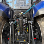 Tractor front cab interior with hydraulic control levers, hoses, and a central joystick; large tires are visible on both sides.