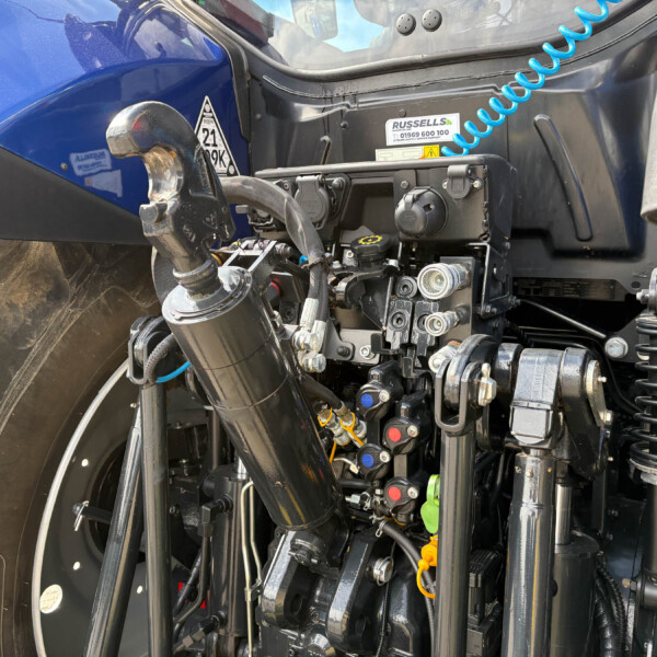 Close-up of a tractor cab interior showing hydraulic levers, hoses, and control modules near a blue body panel.
