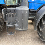 Close-up of a tractor's entry steps and a large front tire, with dirt on the black plastic step and surrounding machinery pieces