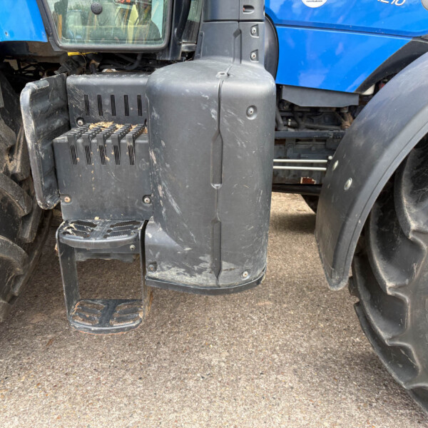 Close-up of a tractor's entry steps and a large front tire, with dirt on the black plastic step and surrounding machinery pieces