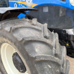 Close-up of a large dirt-covered tractor tire with a blue tractor body in the background, showing treads and wheel hub.
