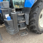 Close-up of a blue tractor showing ladder steps, hydraulic unit, and a large off-road tire.