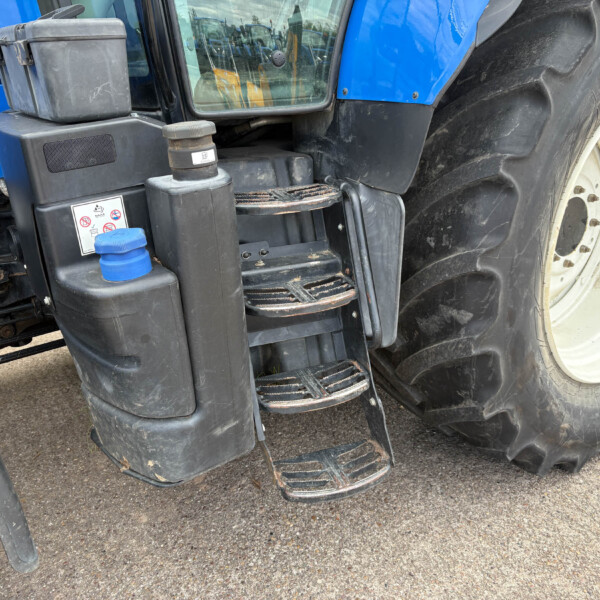 Close-up of a blue tractor showing ladder steps, hydraulic unit, and a large off-road tire.