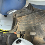 Blue fabric car seat inside a dusty vehicle cab with two foot pedals and a dirty floor mat