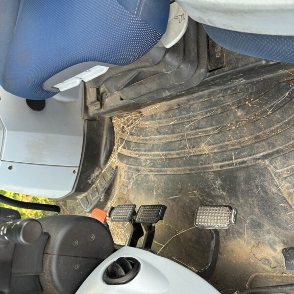 Blue fabric car seat inside a dusty vehicle cab with two foot pedals and a dirty floor mat