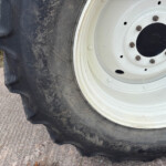 Close-up of a tractor wheel: large off-ground tire with mud, white rim, and bolts visible.