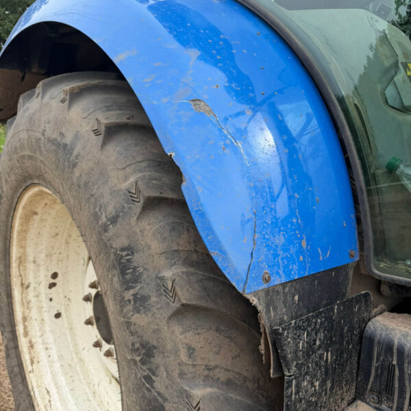 Close-up of a blue tractor fender with a large scratch/crack beside a muddy tire.