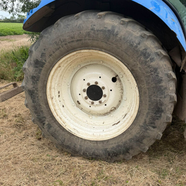 Close-up of a large tractor rear tire with a blue fender in a rural field, showing a dusty white rim and muddy treads.