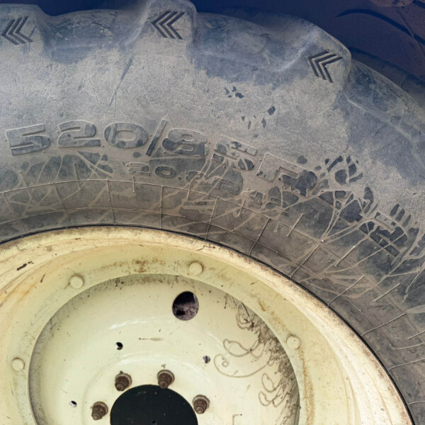 Close-up of a dusty tire mounted on a light-colored wheel, showing tread and dirt splatters on both rim and tread surfaces.