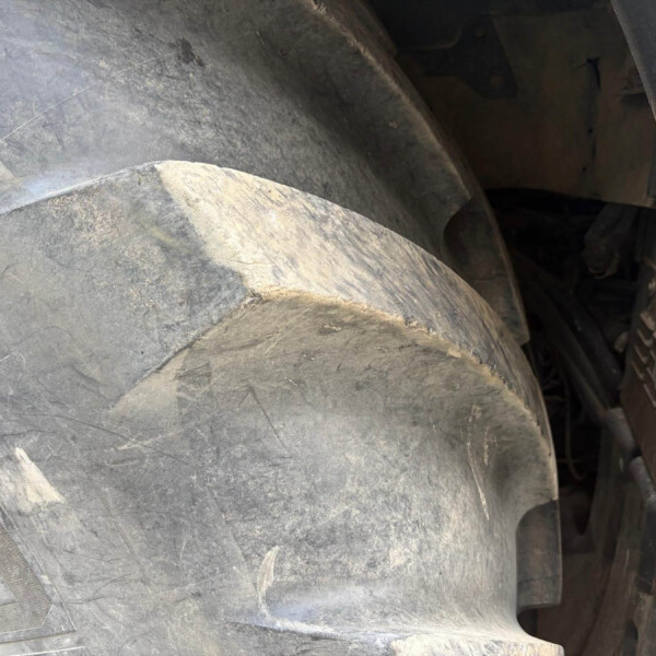 Close-up of a dusty, weathered tire tread with dirt and a glimpse of the rim edge on the right side.