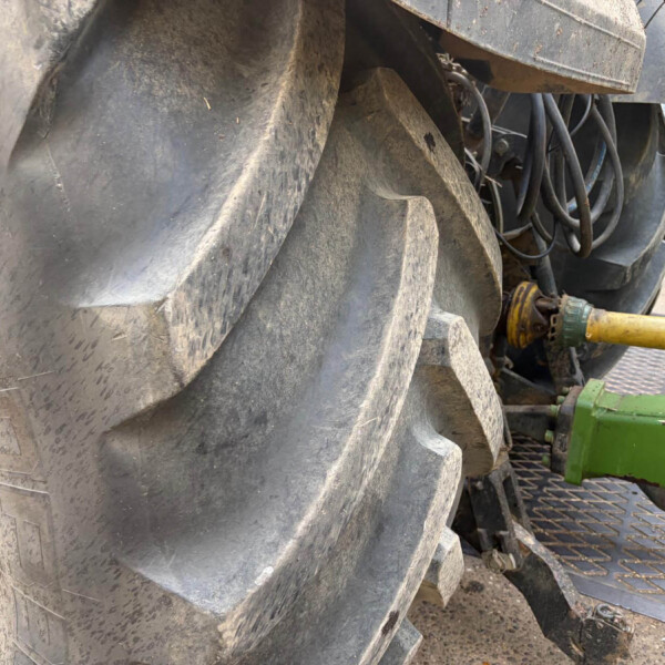 Close-up of large, dirt-covered tractor tires with hoses and industrial equipment in the background