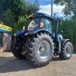 Blue New Holland tractor on display outside a farm store, with a bold yellow-and-blue Russell's sign on the building to the left.