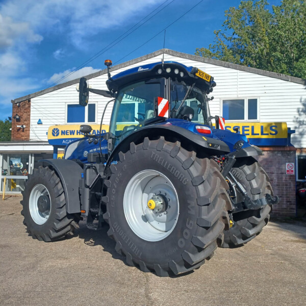 Blue New Holland tractor with oversized tires parked outside a dealership building with a New Holland Agriculture sign.