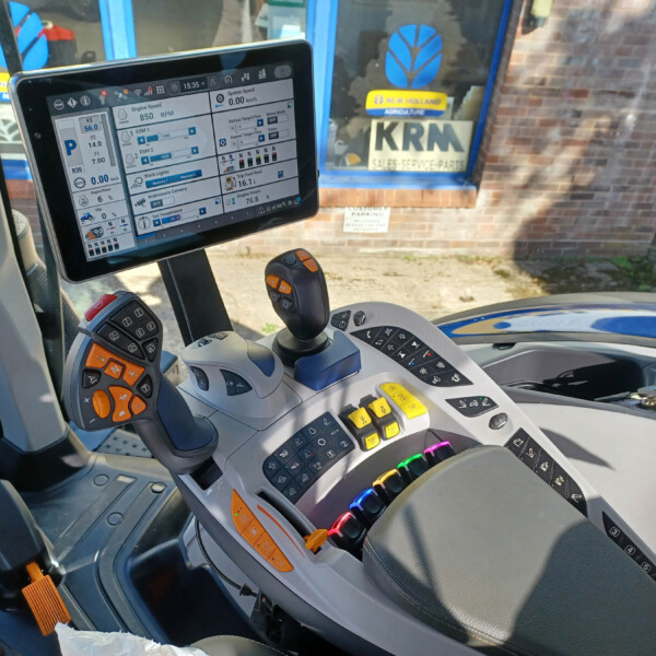 Close-up of a tractor cockpit with a large touchscreen monitor and colorful controls on both sides of the steering column