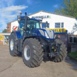 Blue tractor with huge tires parked in front of a service shop with Russell's sign on a sunny day.
