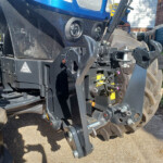 Close-up of a blue heavy construction vehicle’s front, showing two round headlights and exposed hydraulic components.
