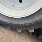 Close-up of a white wheel rim and black tire resting on a dusty, rocky surface (off-road vehicle).