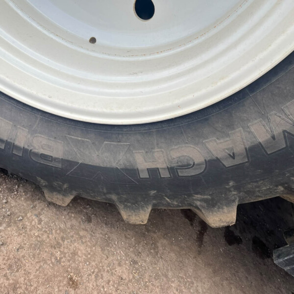 Close-up of a white wheel rim and black tire resting on a dusty, rocky surface (off-road vehicle).